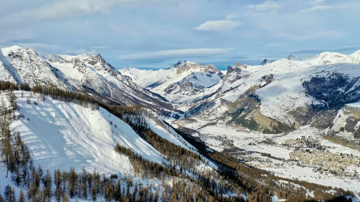Winter view down the larch-forested Guisane valley at Serre Chevalier with pistes cut through the trees and a village on the valley floor