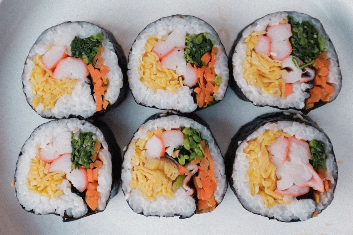 Sei rotoli di kimbap visti dall'alto su un piatto chiaro, il ripieno colorato in evidenza