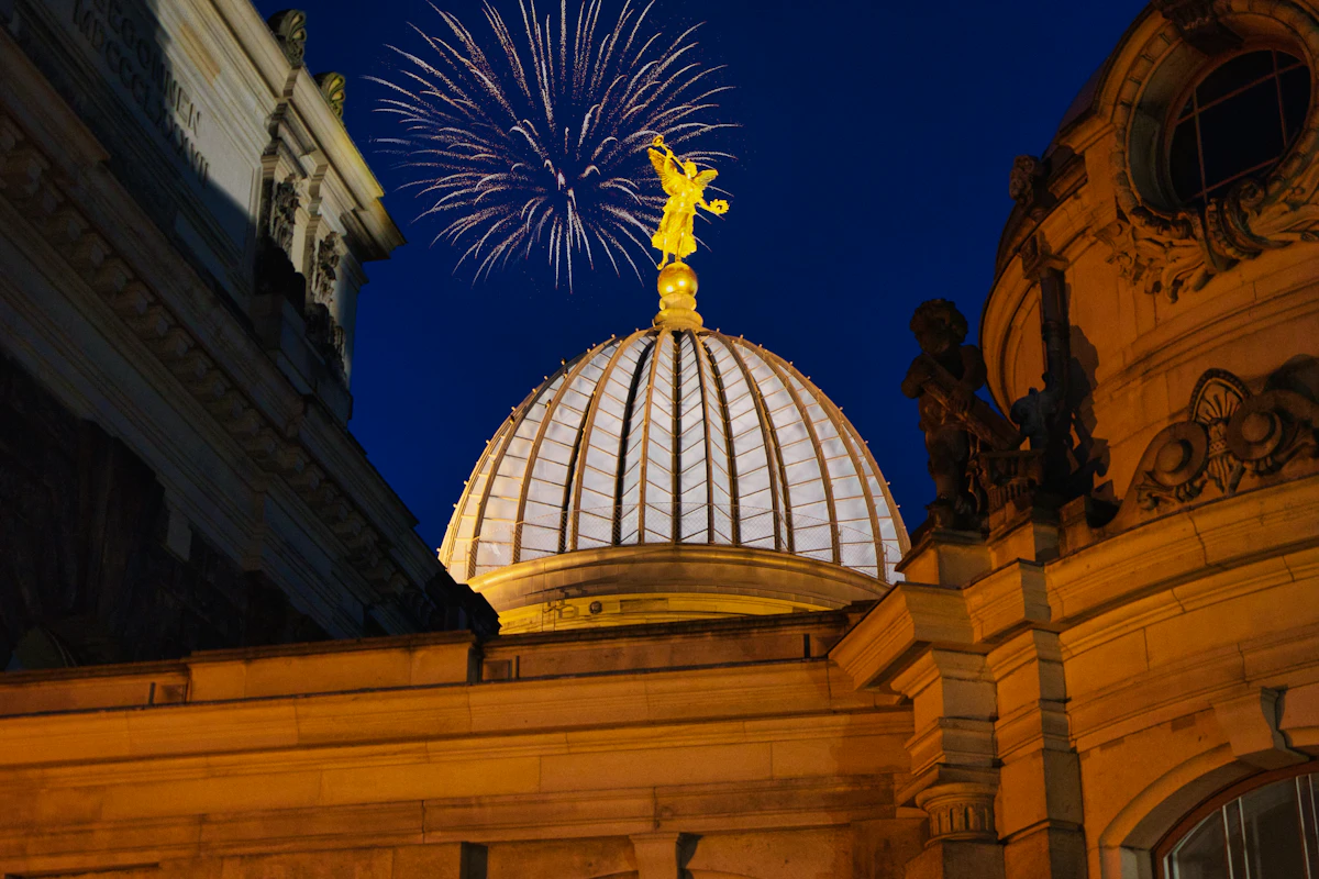 Fireworks bursting in a dark blue sky above a floodlit domed historic building