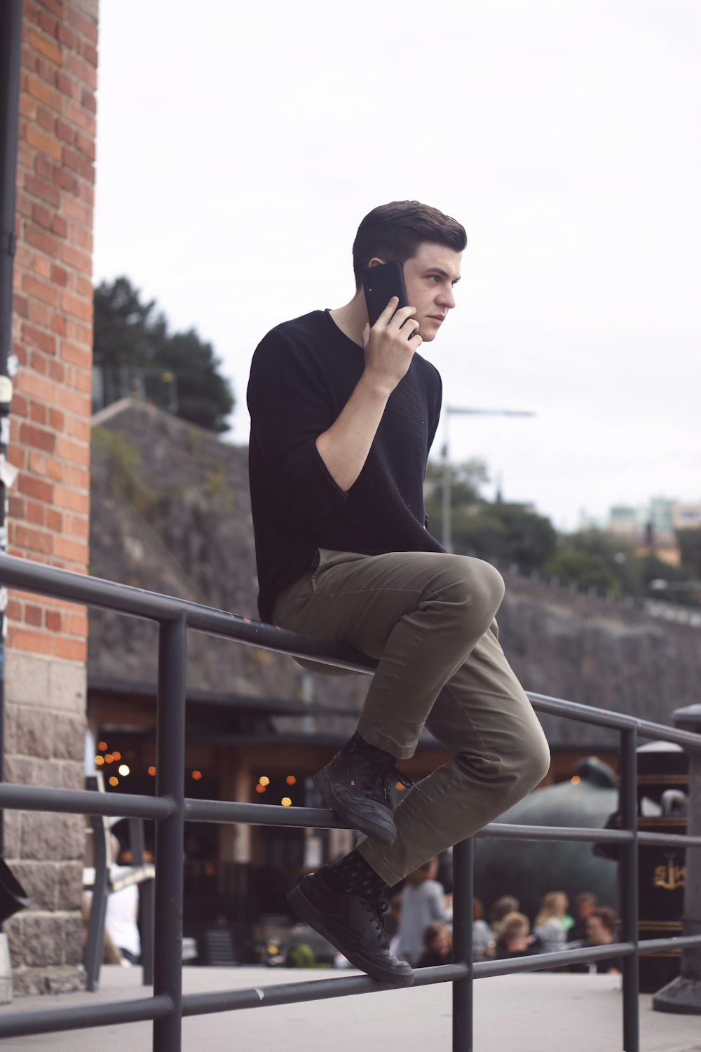 man in black long sleeve shirt and gray pants sitting on black metal railings during daytime