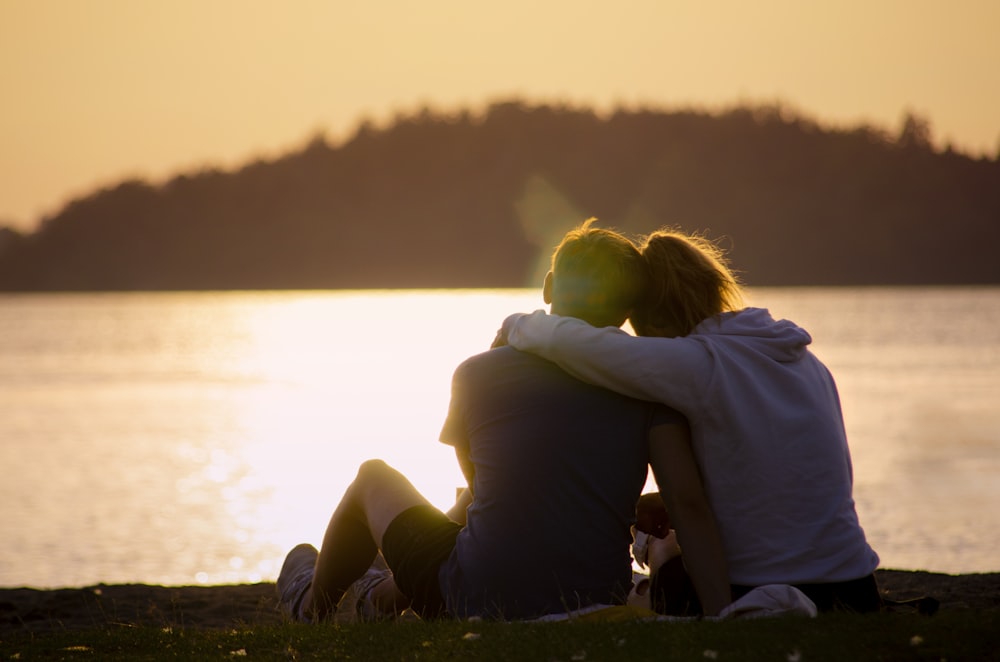 woman in black jacket sitting on green grass field near body of water during daytime