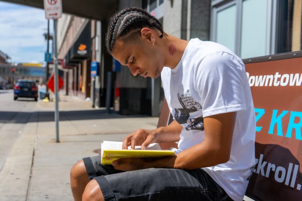 man in white crew neck t-shirt and black denim shorts sitting on bench