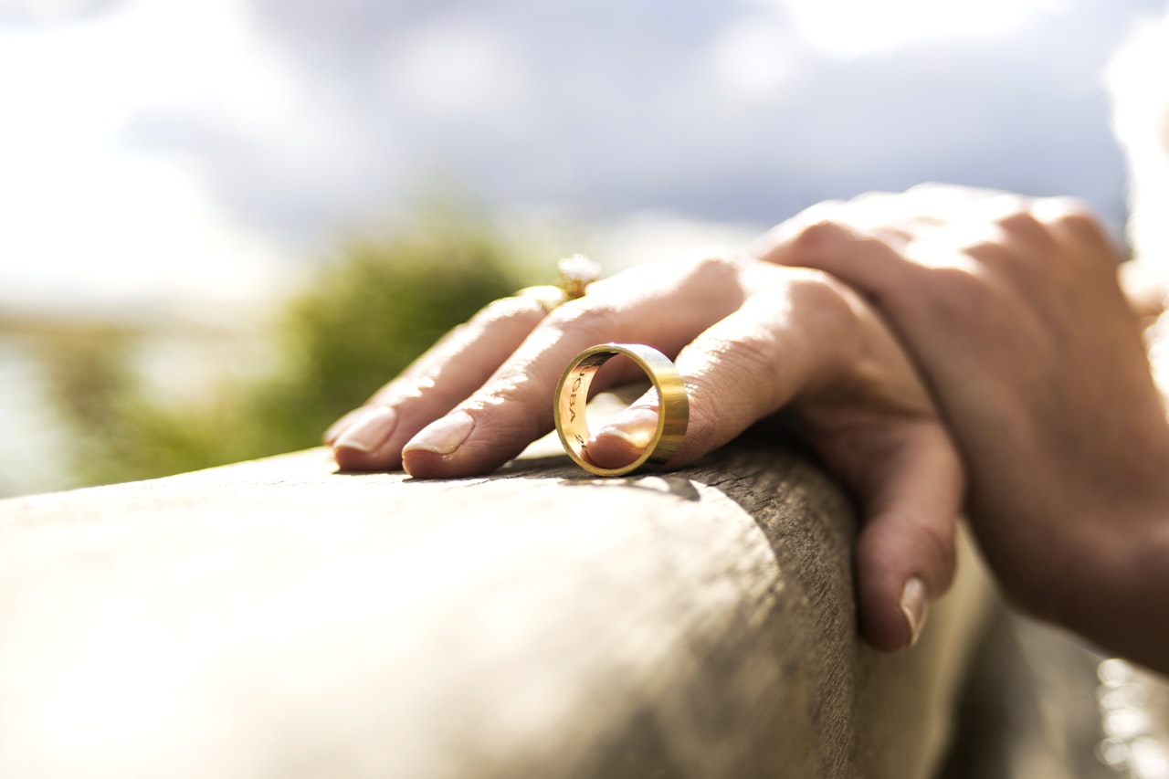 a hand with a gold wedding ring on its ring finger, placed on a brown wooden railing