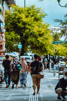 A person wearing a portable air quality monitor while walking through a tree-lined city street on a sunny day.