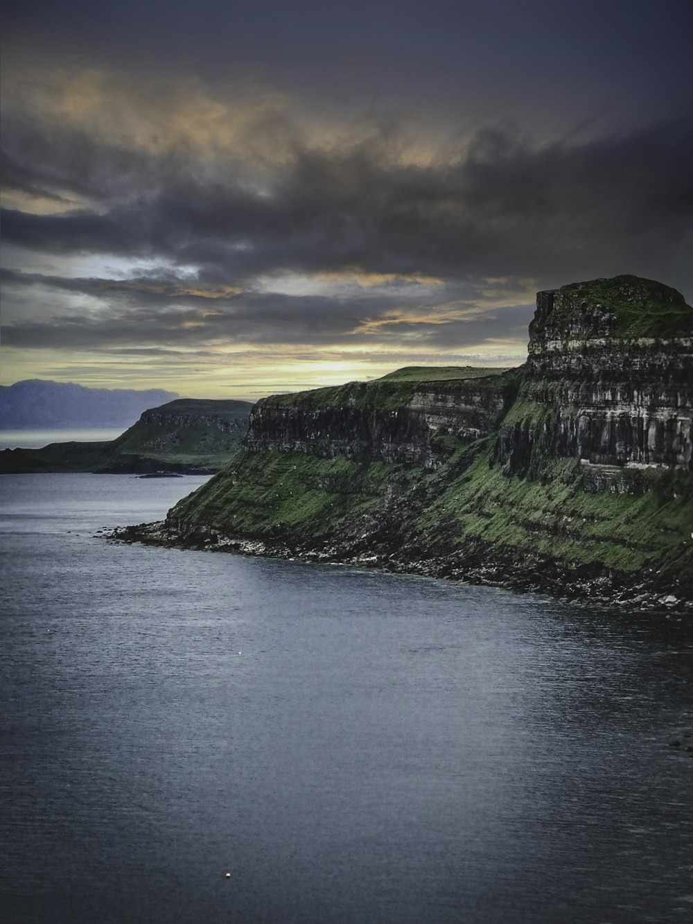 green and gray mountain beside body of water under cloudy sky during daytime