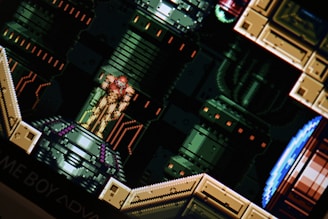 A pixelated scene from a video game featuring a character in a futuristic suit standing on a platform. The background consists of industrial, mechanical designs with pipes and panels.