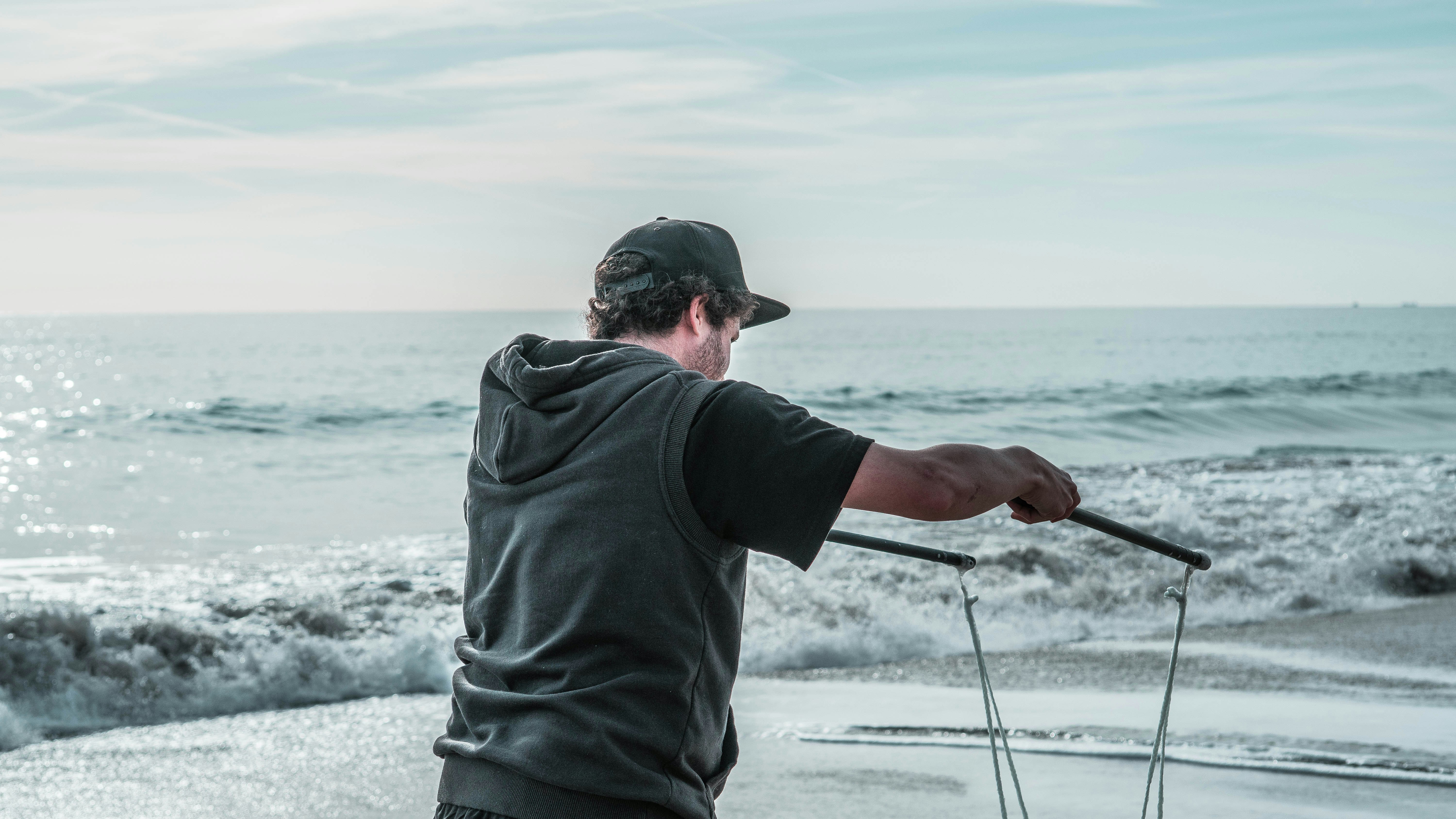 man in black hoodie and black cap holding black fishing rod