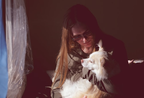 woman in black framed eyeglasses kissing white short coated dog