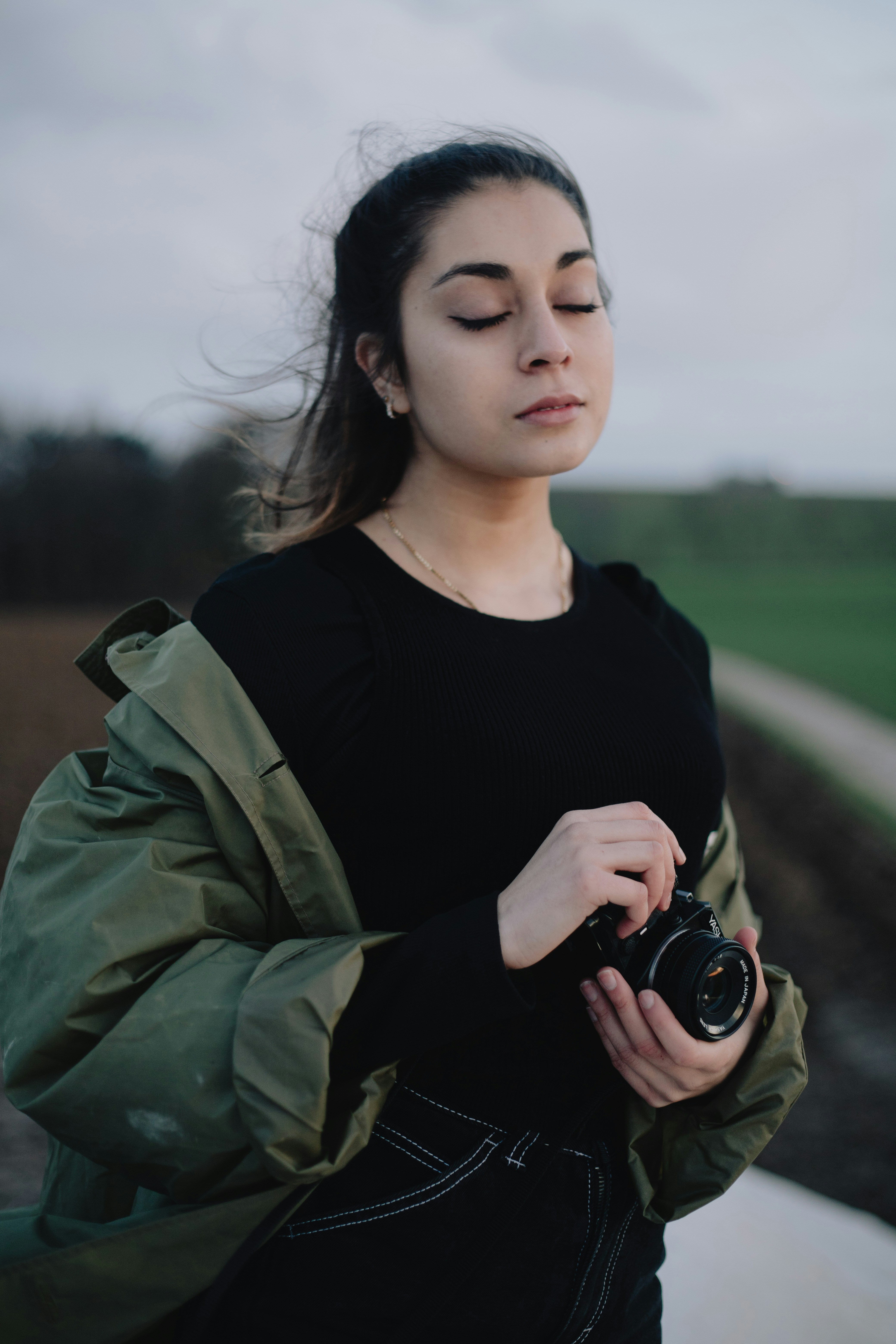 woman in black crew neck shirt and green jacket holding black dslr camera