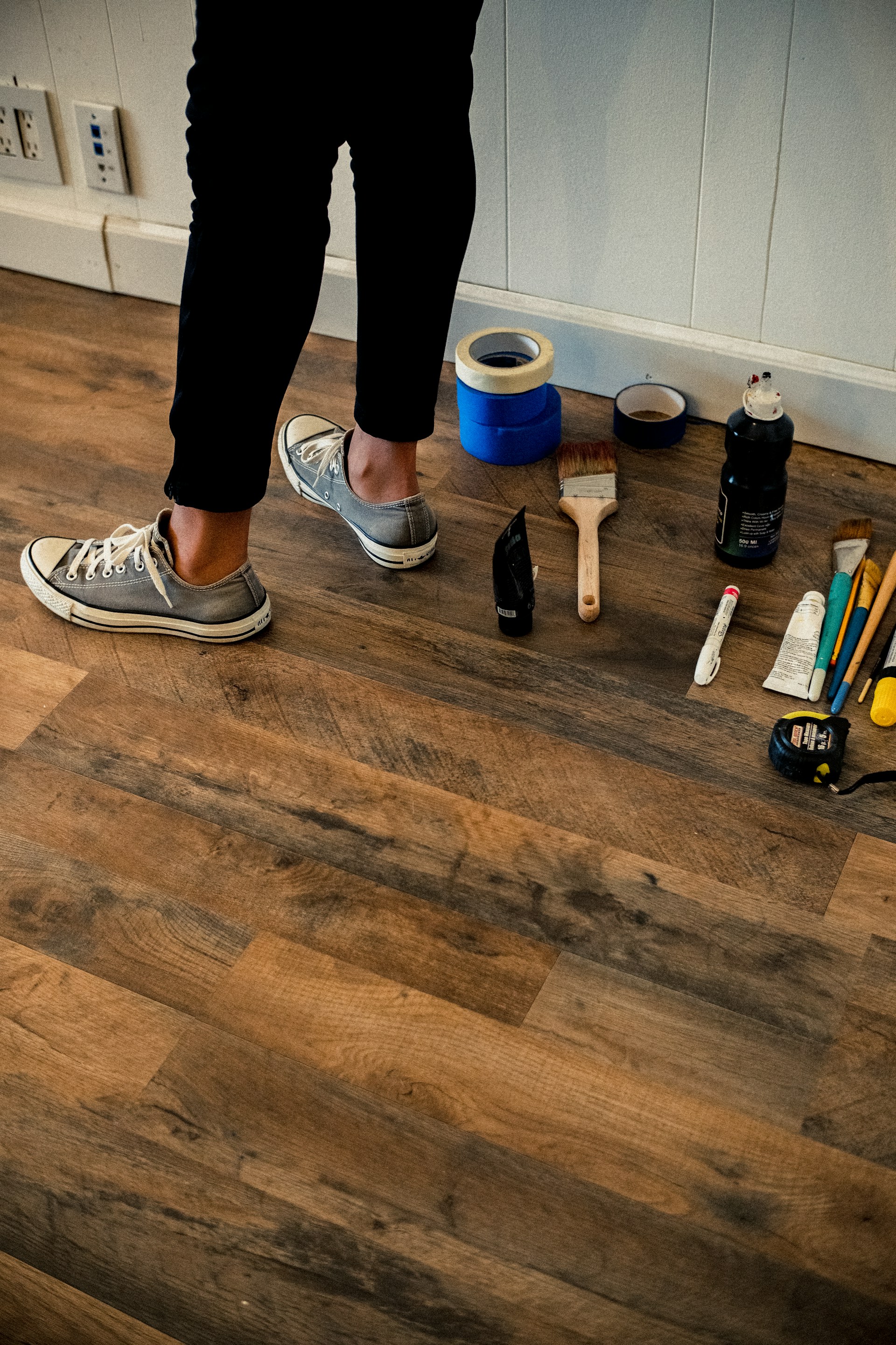 person in black pants and white and black nike sneakers standing on brown wooden floor