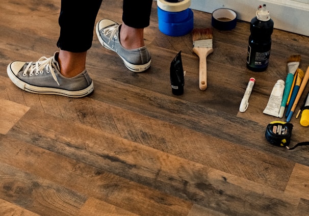 person in black pants and white and black nike sneakers standing on brown wooden floor