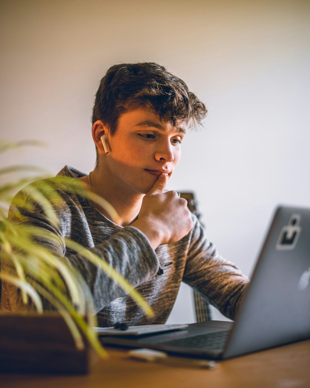 man in grey and black stripe hoodie sitting by the table using silver macbook