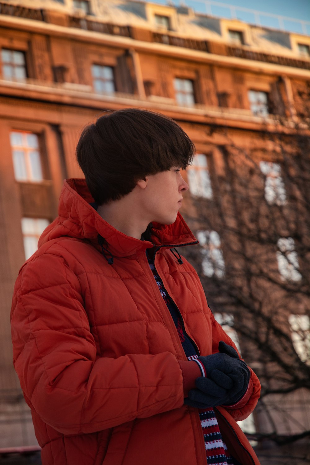 Hombre con chaqueta roja con cremallera de pie cerca del edificio marrón durante el día
