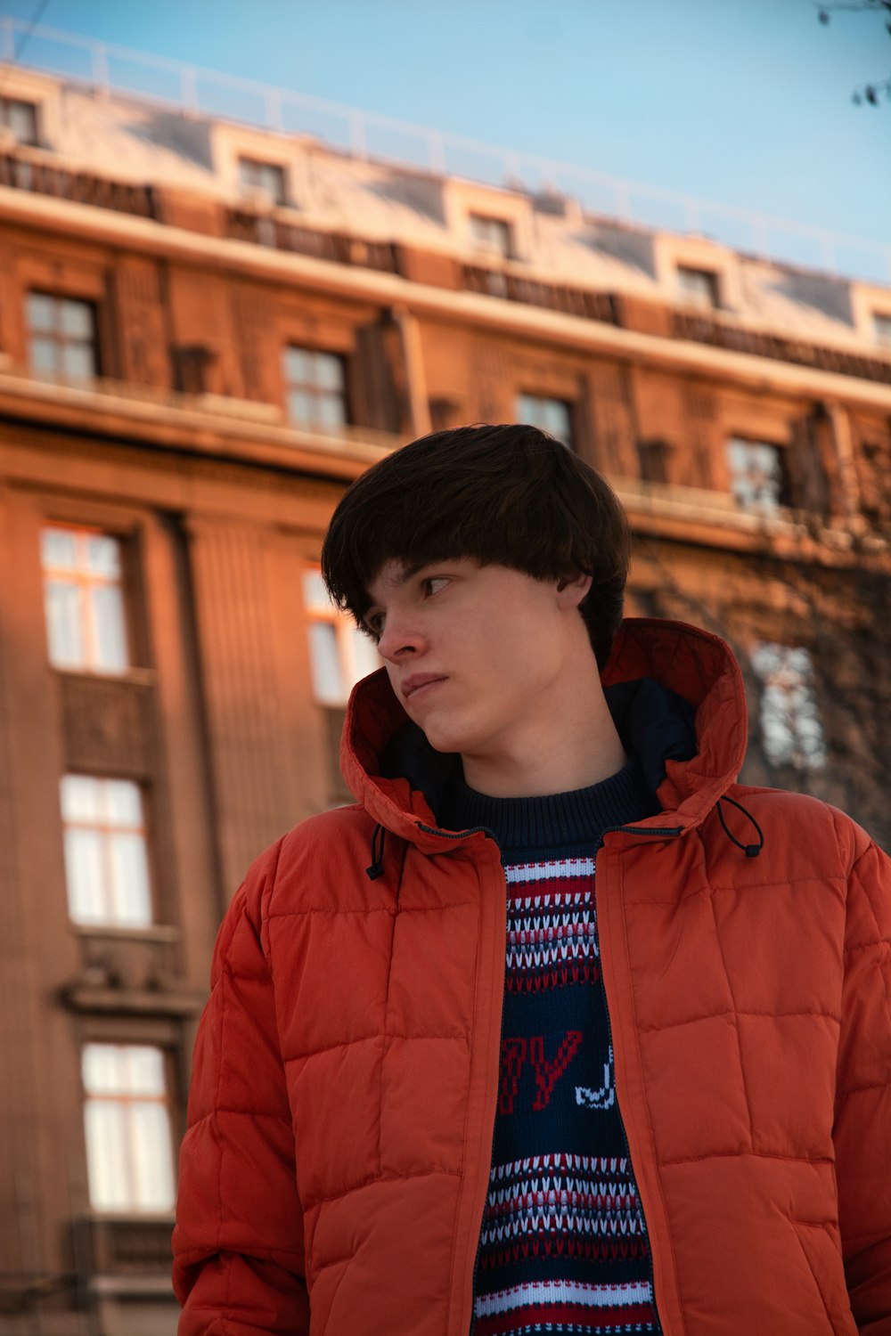 boy in red hoodie standing near brown building during daytime