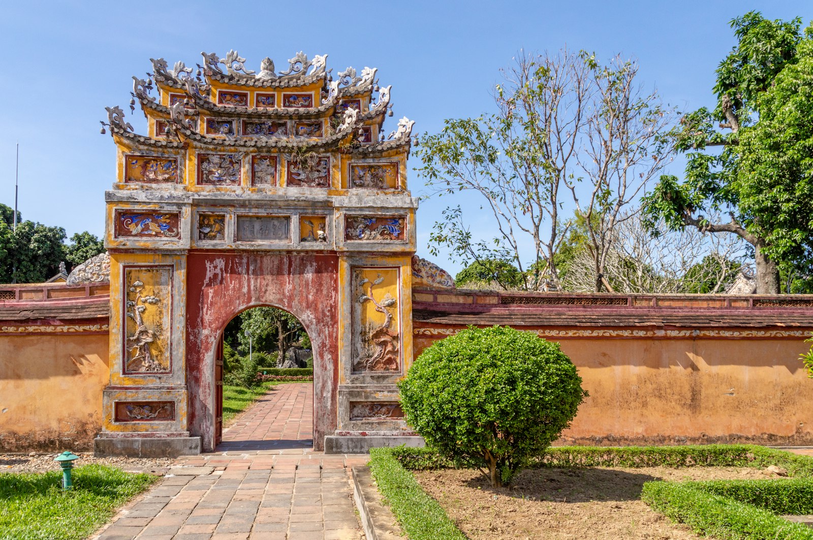 An ornate gate and red wall inside Hue's Imperial City, with a garden path leading through the arch