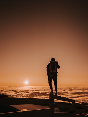 silhouette of man standing on wooden dock during sunset