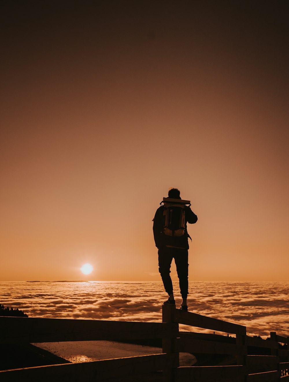 silhouette of man standing on wooden dock during sunset