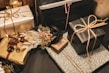 Multiple gift boxes are wrapped in elegant paper with a variety of colors and textures. The packages feature intricate patterns and some are tied with simple twine. A small dried floral arrangement adds a touch of rustic charm to one of the gifts.