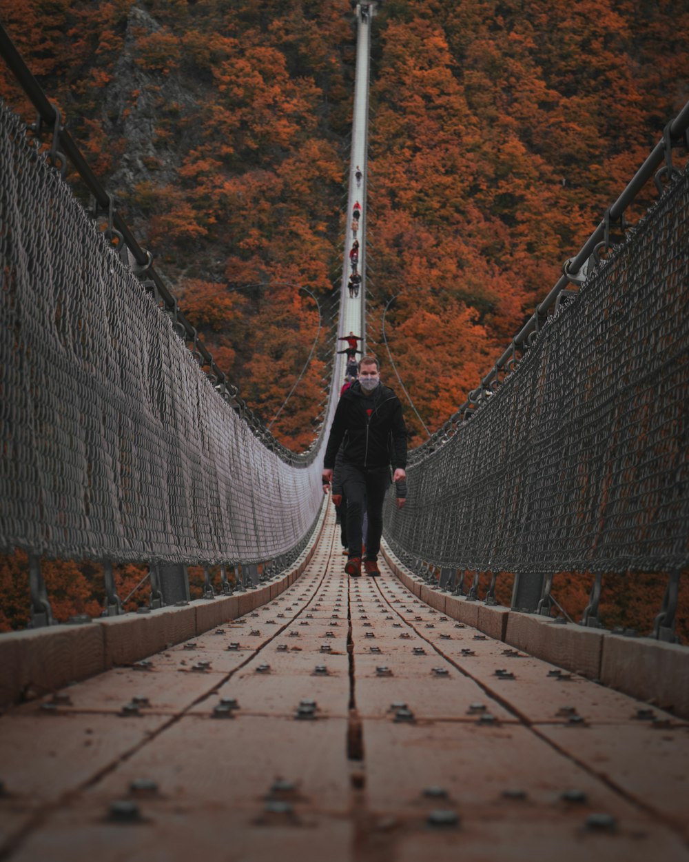 person in black jacket walking on hanging bridge during daytime