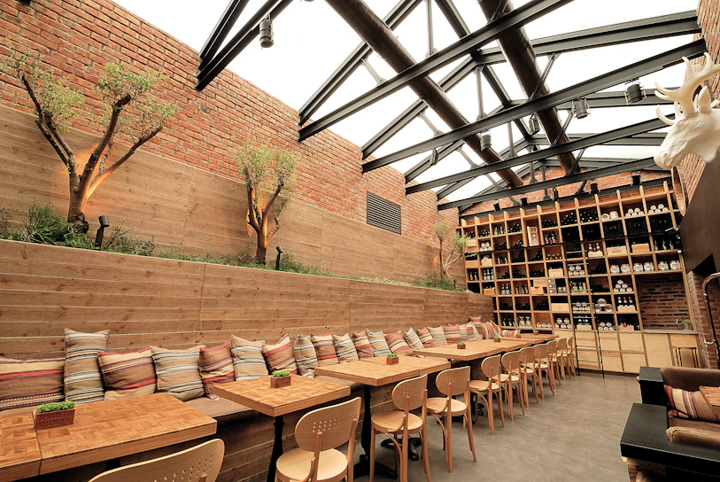 Warm, natural light floods a cozy Scandinavian-style restaurant interior with wooden tables and deep crimson accents.