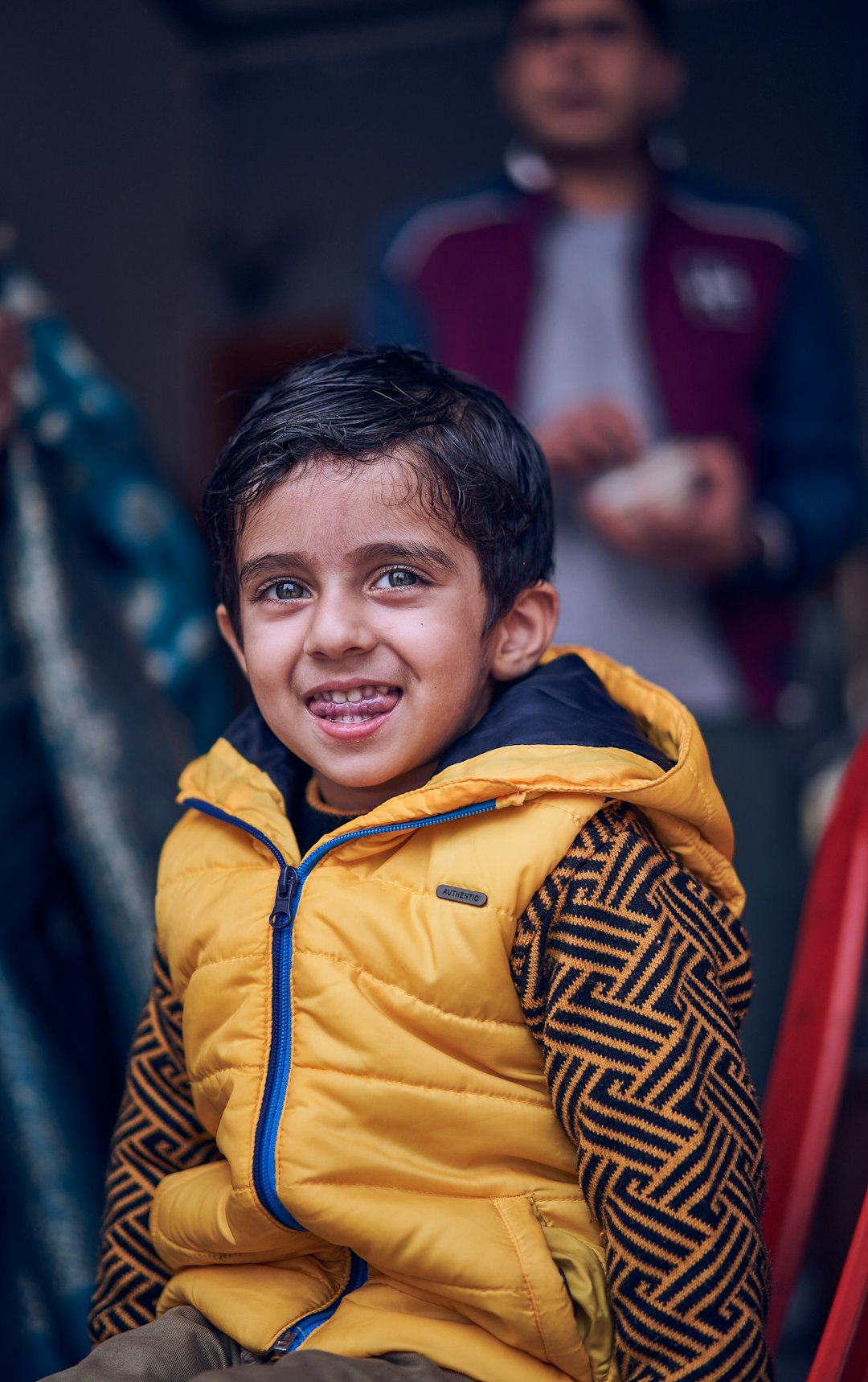 boy in yellow and blue zip up jacket smiling