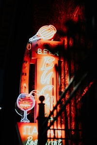 A brightly lit neon sign displaying the words wine, beer, and restaurant. The sign features images of a wine glass and a beer mug in vibrant neon colors, creating a warm and inviting glow in the darkness.