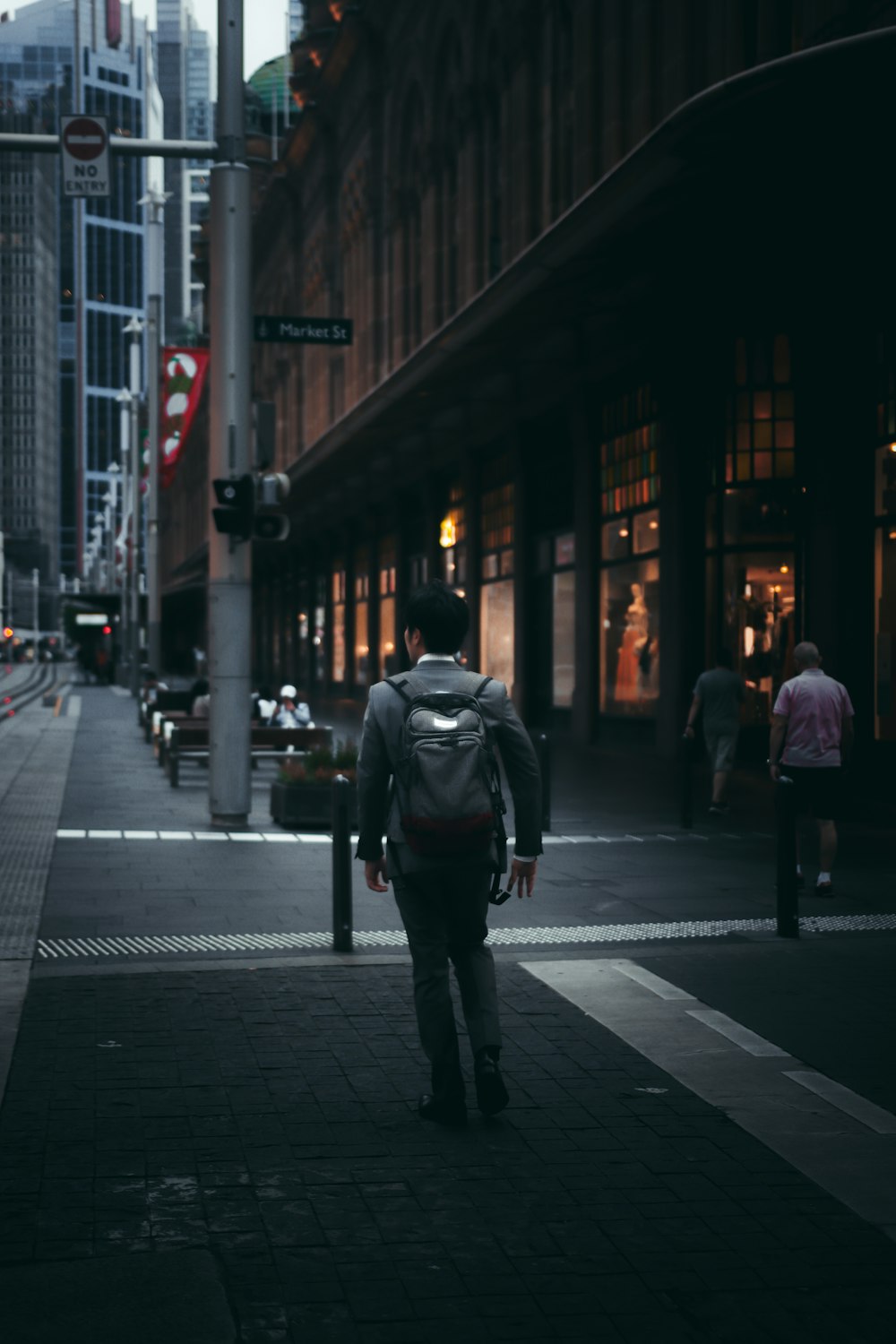 uomo in giacca nera che cammina sul marciapiede durante la notte