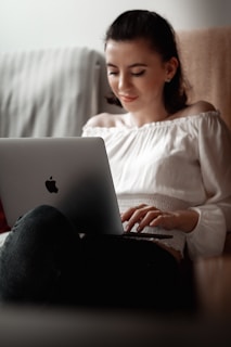 woman in white long sleeve shirt and black pants sitting on bed using macbook