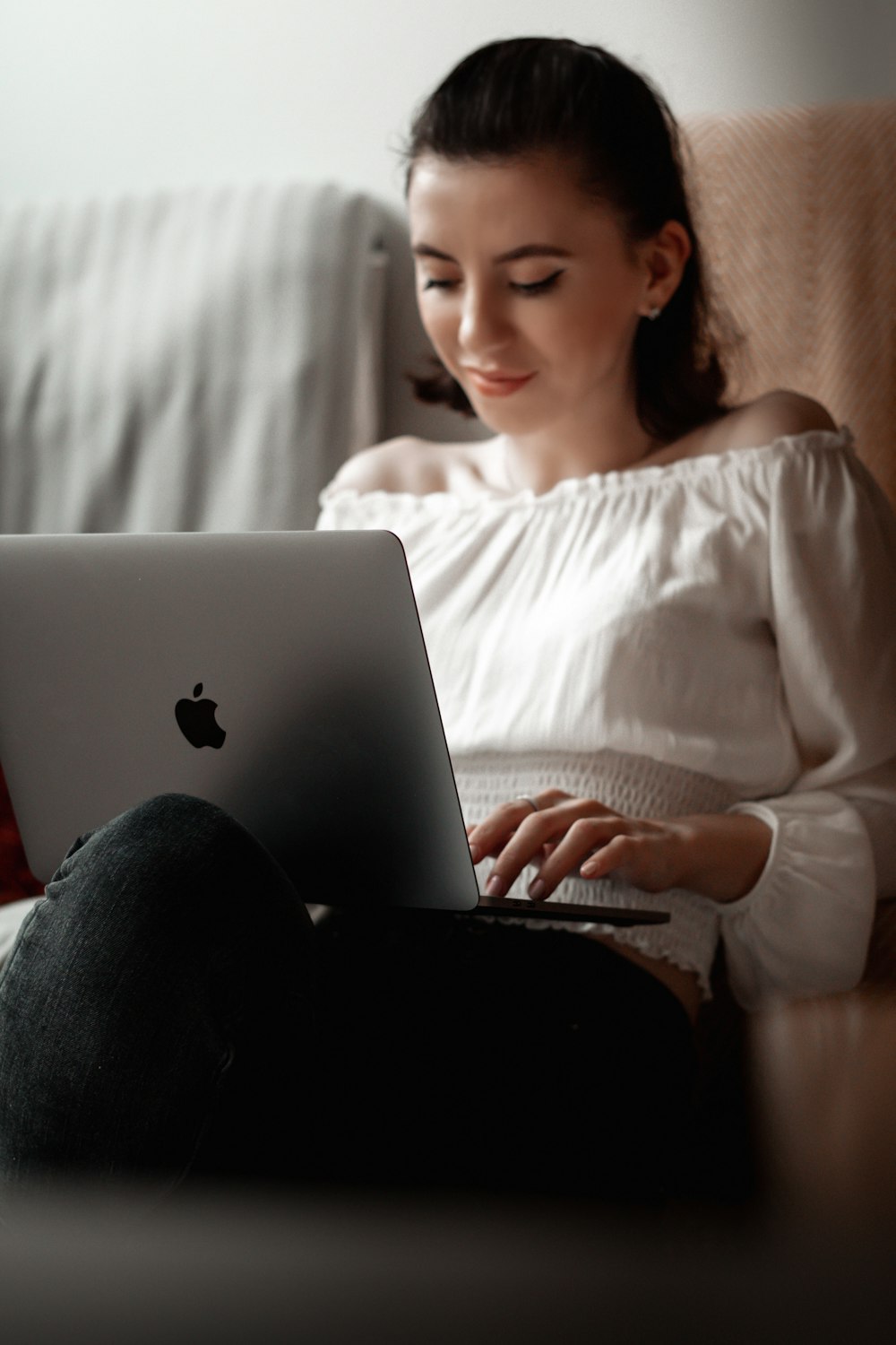 흰색 긴 소매 셔츠와 검은 색 바지를 입은 여자가 MacBook을 사용하여 침대에 앉아