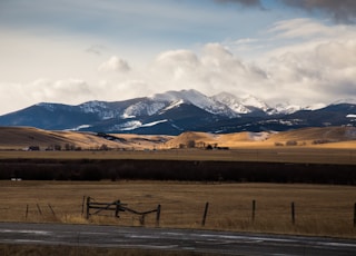 brown field near mountains under white clouds during daytime