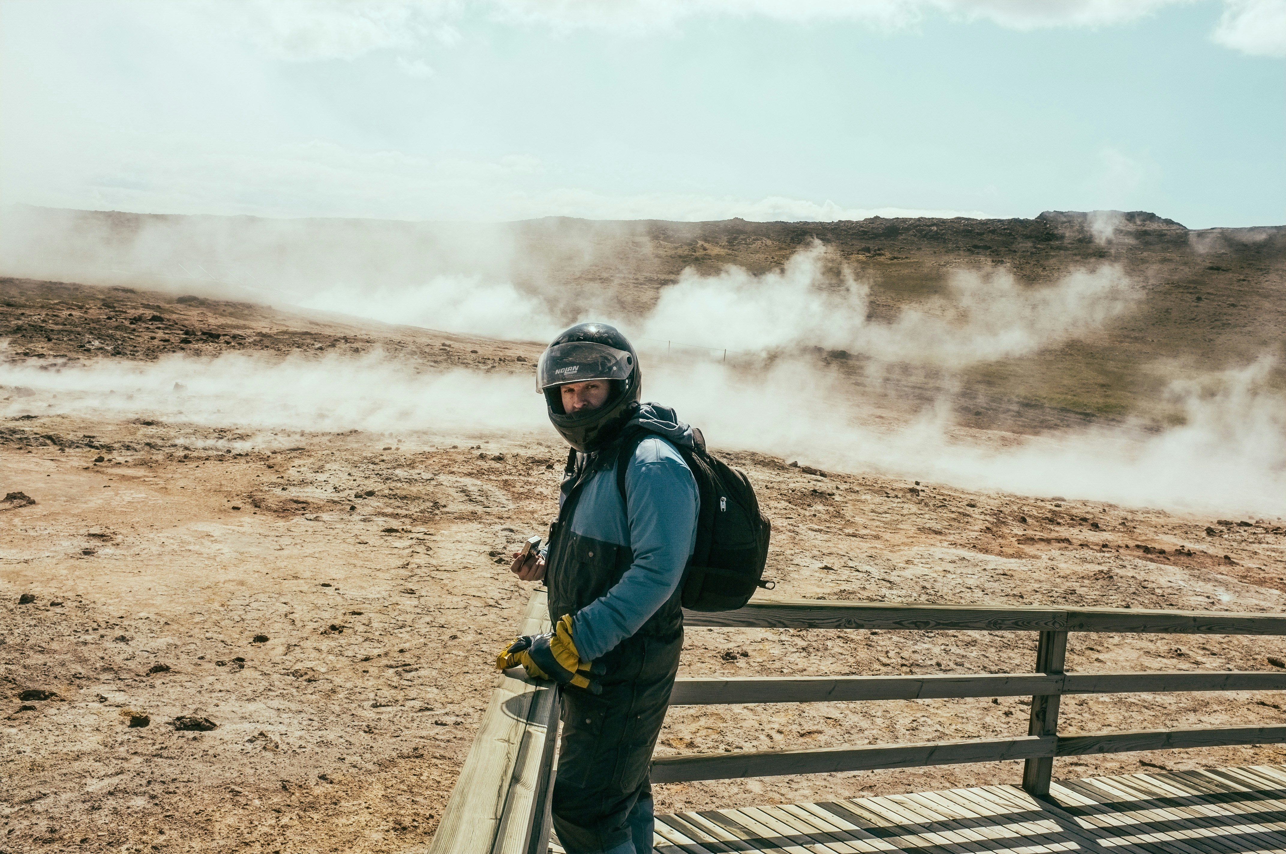 man in blue jacket and yellow backpack standing on brown wooden fence during daytime