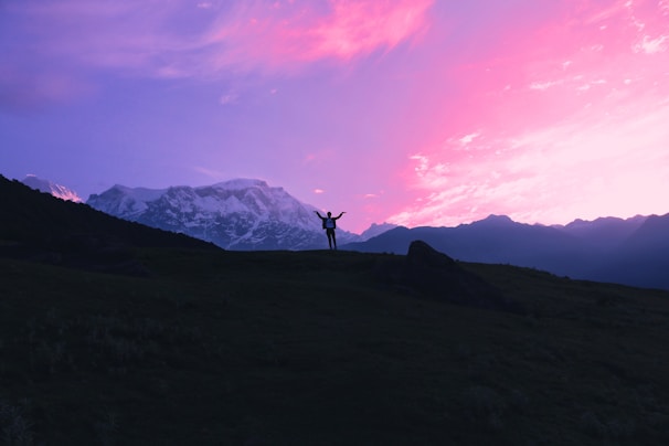 Sunset silhouette of a person wearing a Kingdomcraft hoodie, standing on a hill with arms raised.