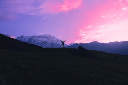 Sunset silhouette of a person wearing a Kingdomcraft hoodie, standing on a hill with arms raised.