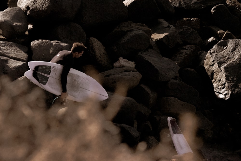 man in black shirt lying on white surfboard on rocky shore during daytime