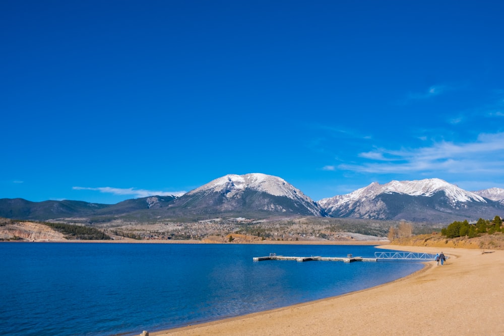 blue body of water near white and black mountain under blue sky during daytime