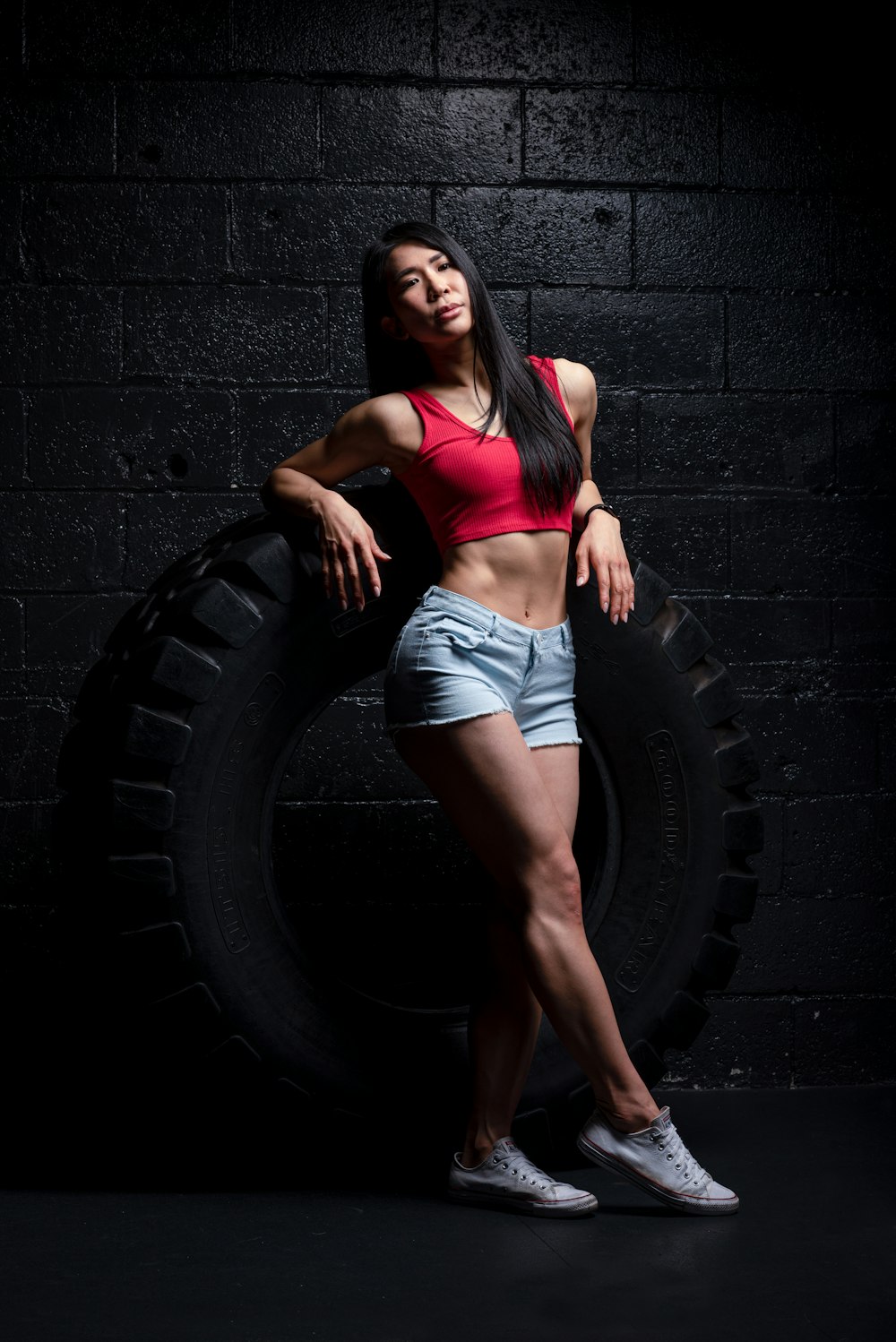 woman in pink sports bra and blue denim shorts leaning on black concrete wall