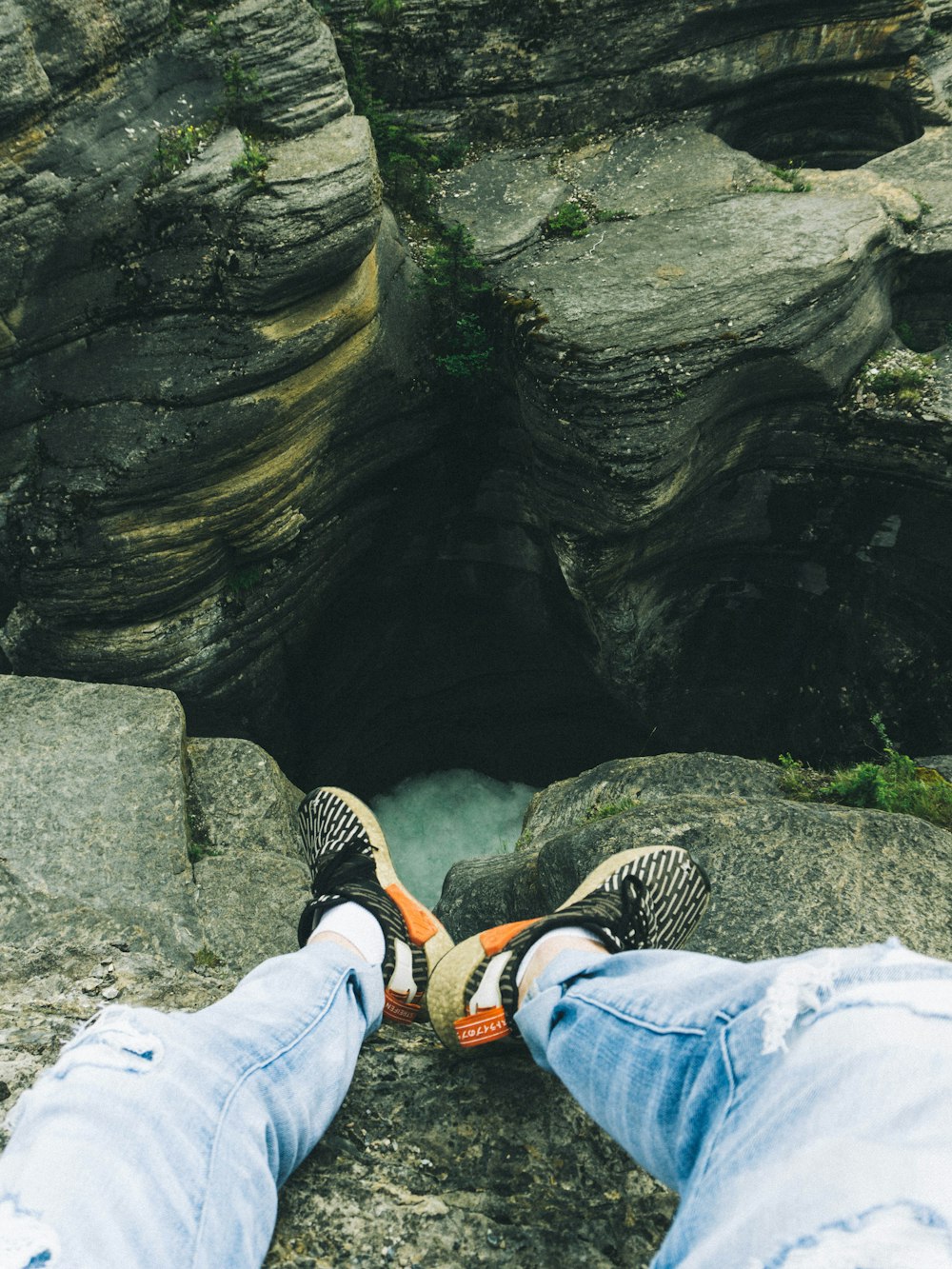 person in blue denim jeans and black sneakers sitting on rock