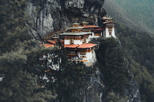 white and brown concrete house on rocky mountain during daytime in Tiger’s Nest/ Takstang Palphug Monastery Bhutan