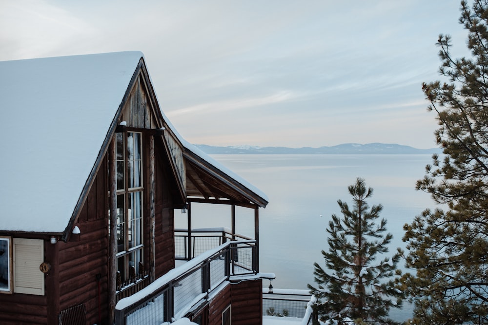 Maison en bois brun sur un sol enneigé près d’un plan d’eau pendant la journée