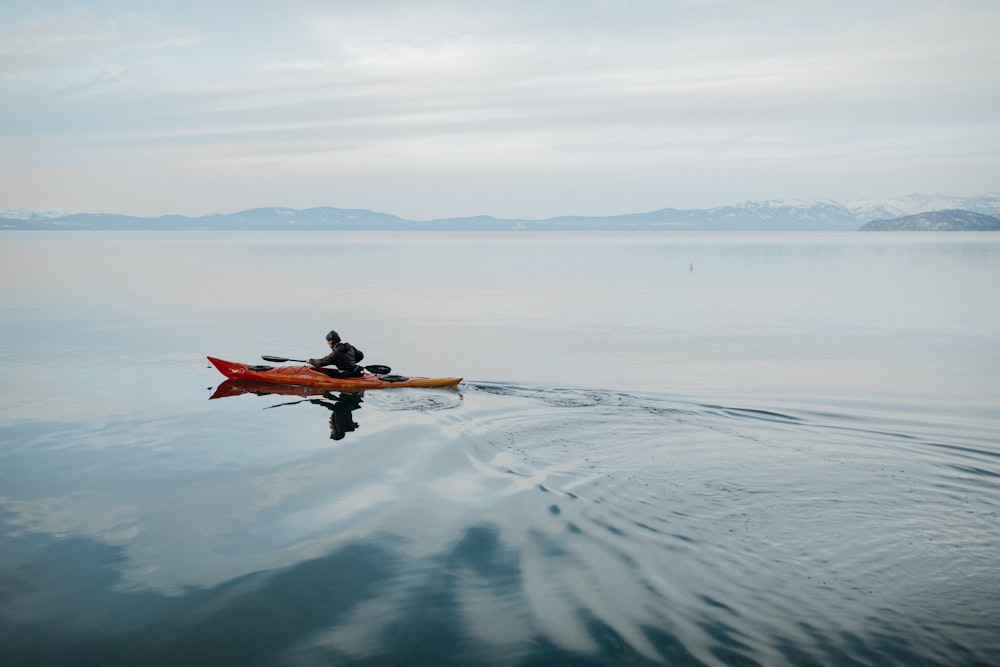 homme en costume rouge et noir montant sur un kayak orange sur la mer pendant la journée