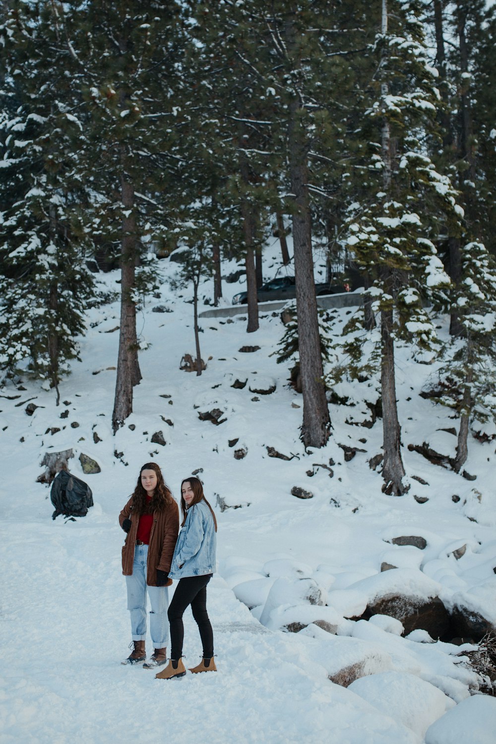 2 women standing on snow covered ground near trees during daytime