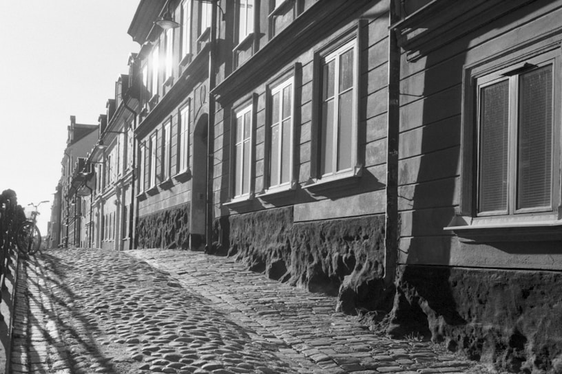 Black and white photograph of a narrow cobblestone street in an Italian village, light casting long shadows.