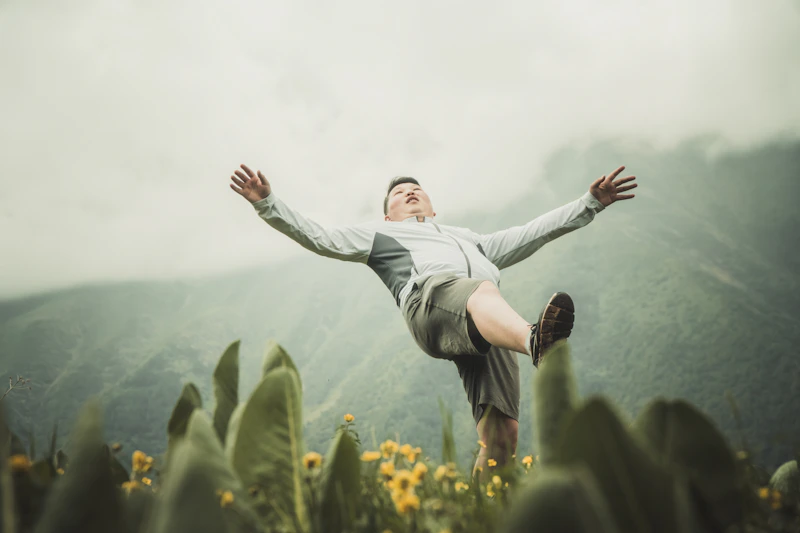 Energetic UK sugar baby in a white long-sleeve shirt and black pants jumping on a green field