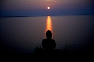 A serene moment of reflection by a student sitting near a peaceful campus pond at sunset.