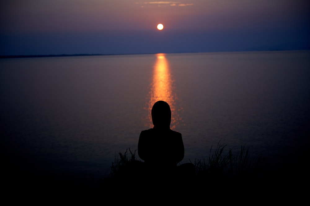 silhouette of person sitting on grass during sunset