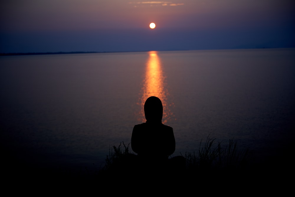 silhouette di persona seduta sull'erba durante il tramonto