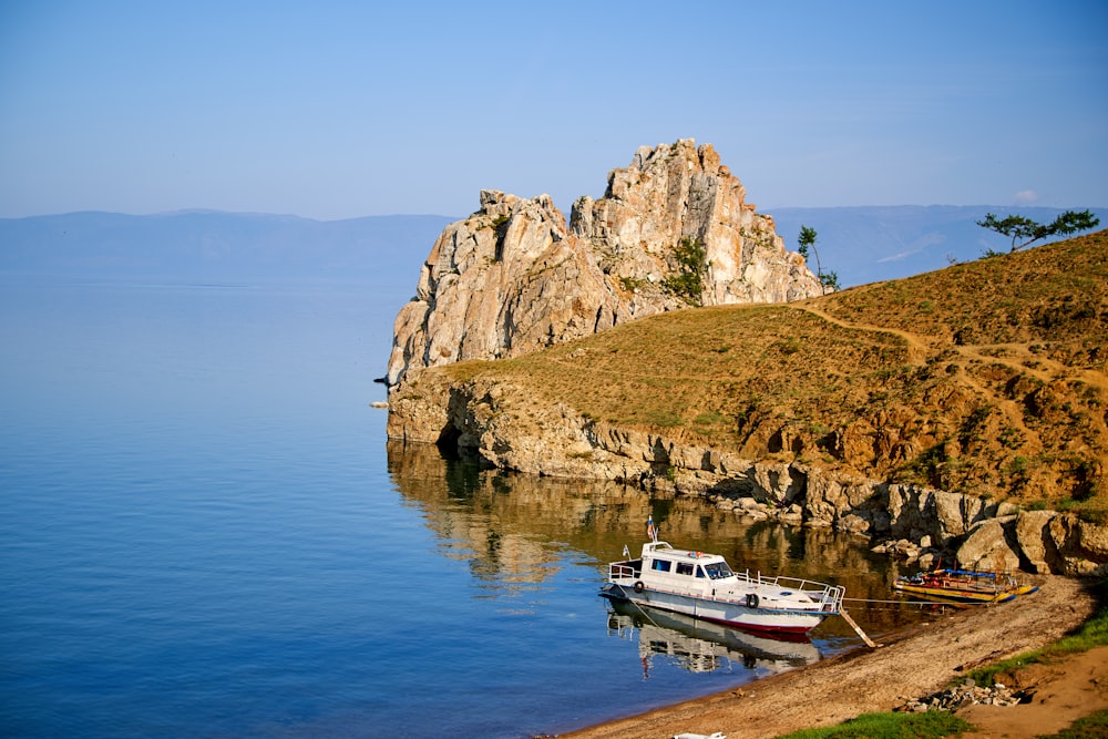 white boat on body of water near brown and green mountain during daytime