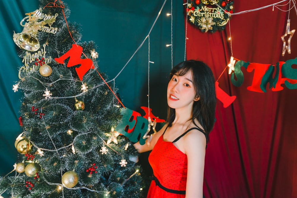 woman in red spaghetti strap dress standing beside green christmas tree