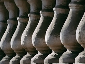 A close-up view of a series of architectural balusters, each displaying curved and symmetrical patterns. The texture of the stone or concrete is emphasized by the interplay of light and shadow across the surface.
