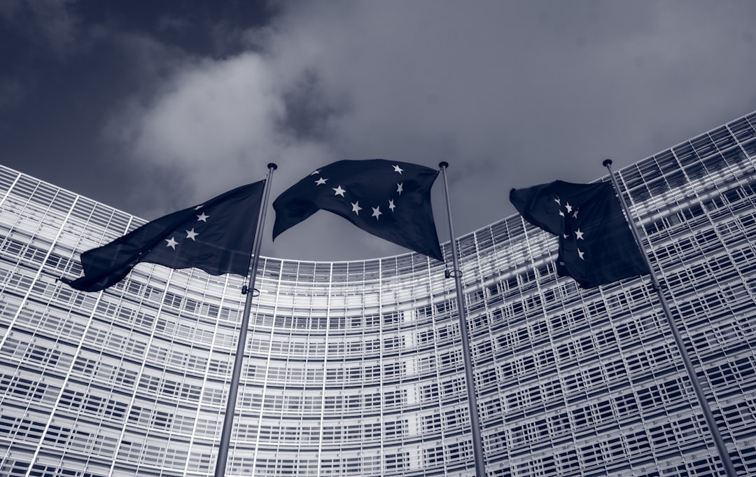 blue flag on pole near building, Flags of the European Union in front of the EU-commission building "Berlaymont" in Brussels, Belgium